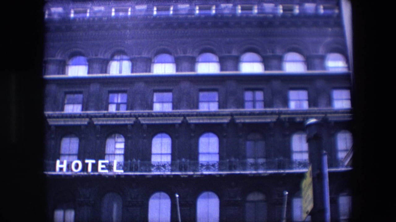 Upper facade of a brick hotel with arched windows and partial illuminated HOTEL sign.
