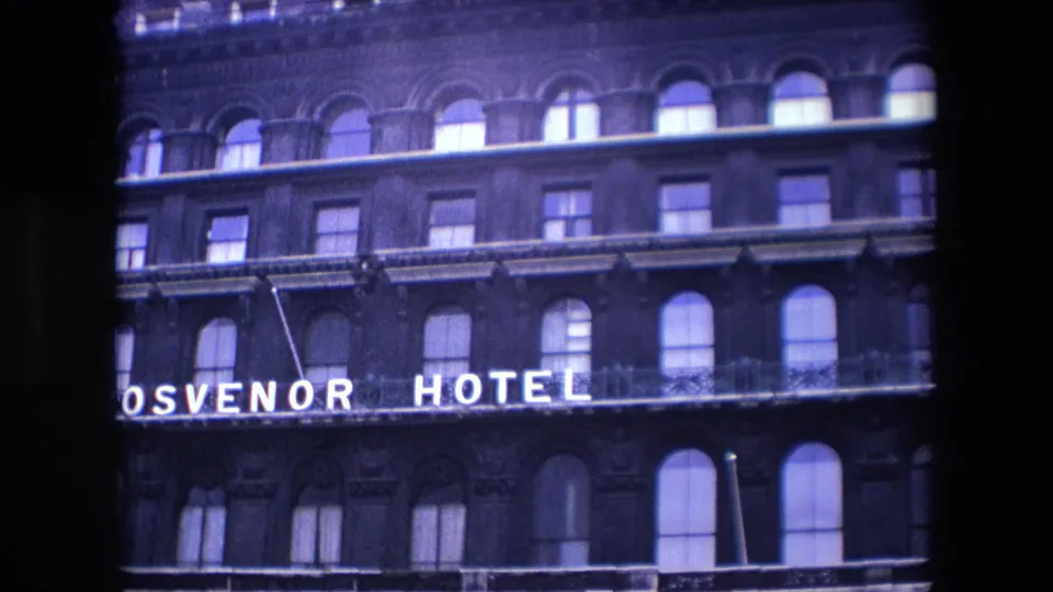 1967 London view of the Grosvenor Hotel facade, showing partial illuminated signage, arched lower windows, upper window rows, and dark brick architectural detail.