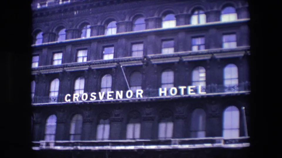 1967 London 8mm frame showing the upper facade of the Grosvenor Hotel with bright lettering across a dark masonry building and repeated arched windows.
