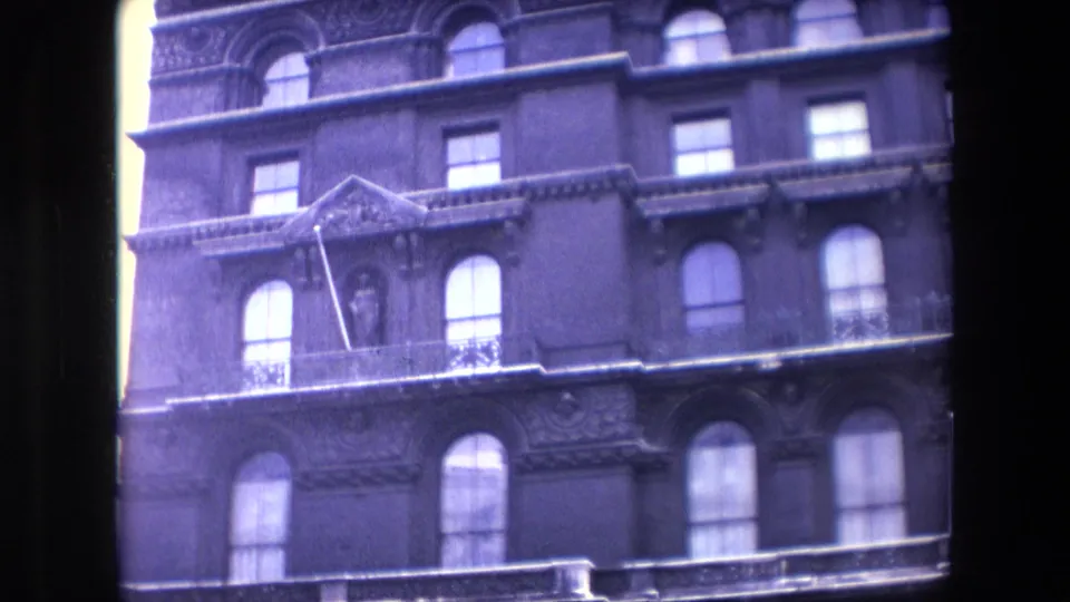 The clip ends on a purple-blue 8mm view of a grand London building facade with arched windows, decorative molding, balconies or ledges, and a mansard-style upper roofline.