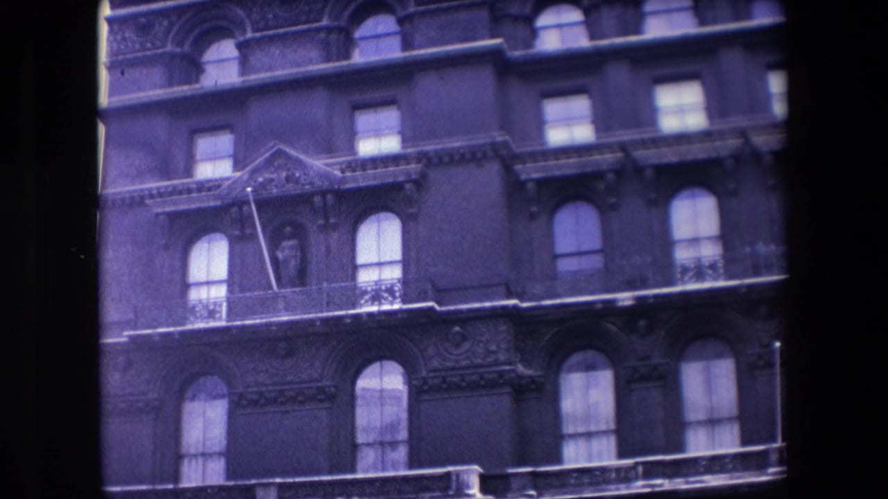 1967 London 8mm frame showing an ornate multi-story facade with arched windows, balcony railings, decorative stonework, and a statue in a niche.
