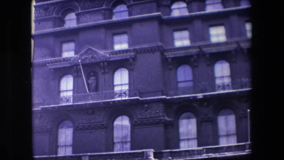 1967 London 8mm frame showing an ornate multi-story facade with arched windows, balcony railings, decorative stonework, and a statue in a niche.