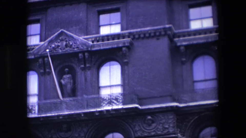 1967 London home-movie frame showing a zoomed-in portion of the ornate building facade with a statue niche, balcony railing, arched windows, and carved architectural detail.