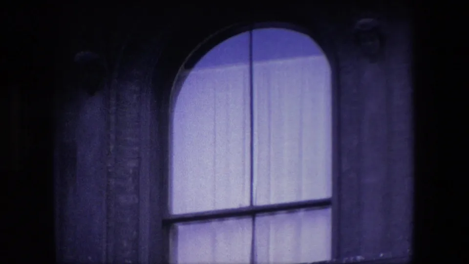 Zoomed 8mm frame from London showing the large arched church window with pale interior curtains, surrounding dark stonework, and partial carved details at the edge.