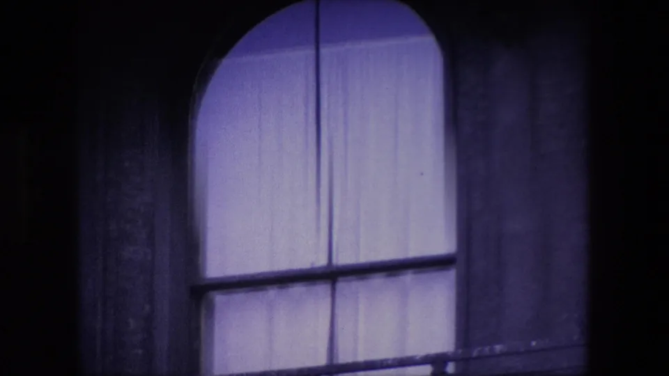 Tight 1967 London home-movie view of the arched church window, pale curtains, stone surround, and dark scanned-film borders.