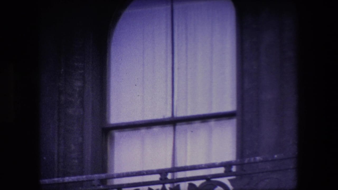 Close 8mm view of an arched curtained window and balcony railing on a dark stone London building, supported by the clip metadata.