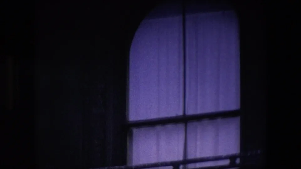 Close-up of a lower arched window with blue-purple curtain, dark architectural framing, and balcony rail detail in the London street sequence.