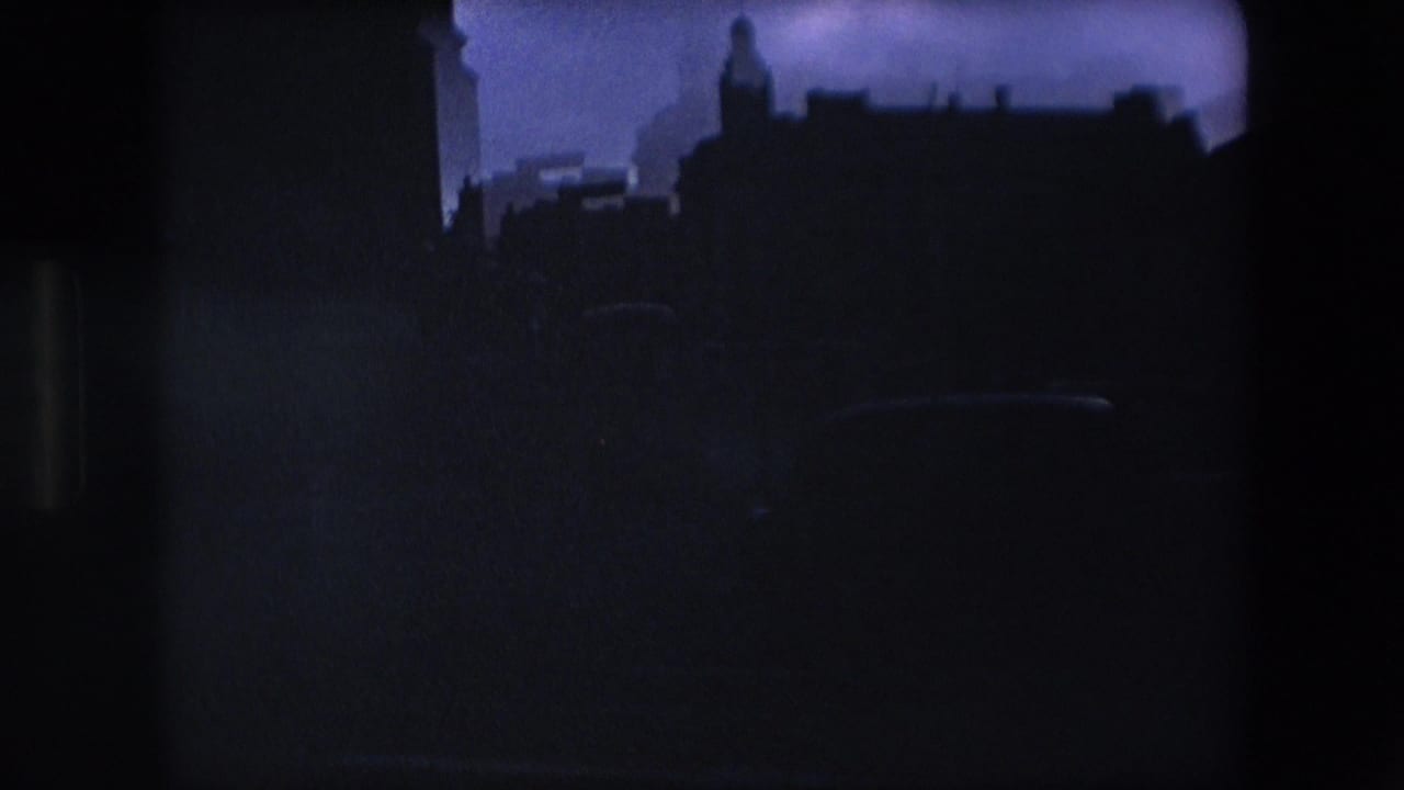 Dark silhouetted city rooftops and buildings against a dim sky.