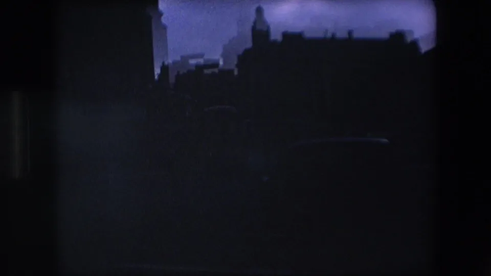 A dark 8mm frame shows silhouetted London building outlines and rooftops against a cool dim sky, with little street detail visible.