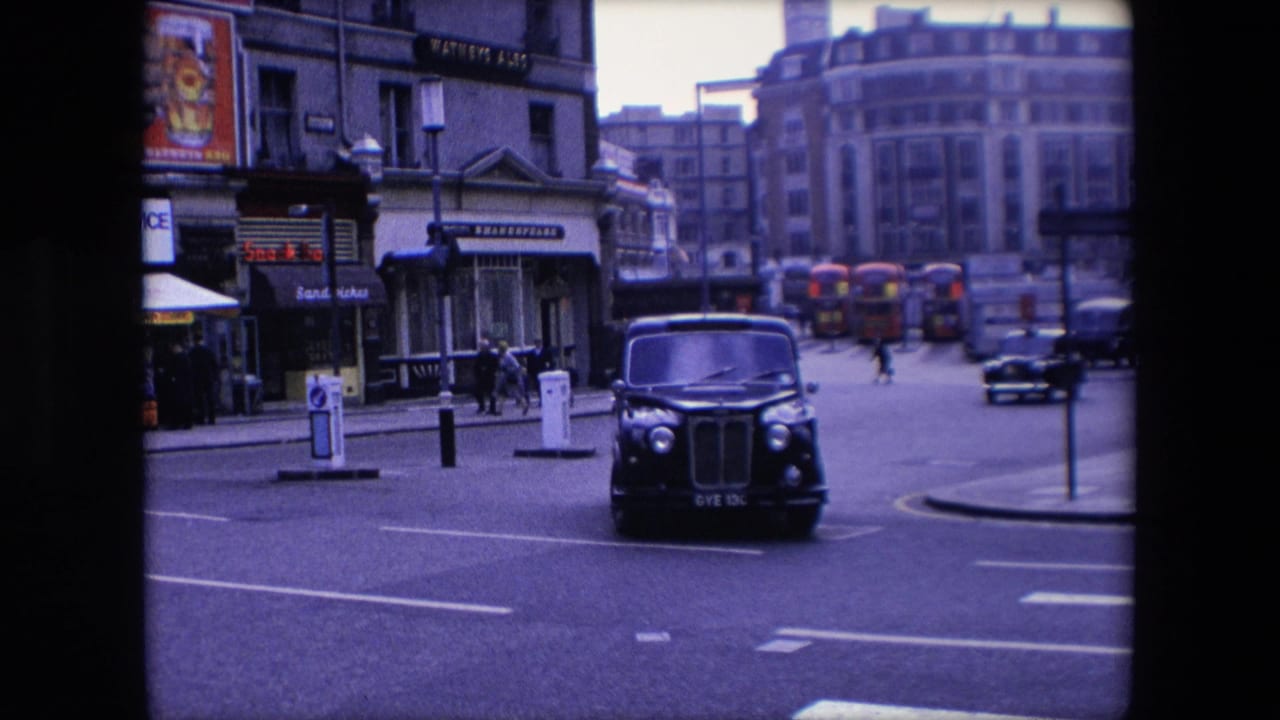 Black taxi turning near a corner with buses and traffic lights in the background.