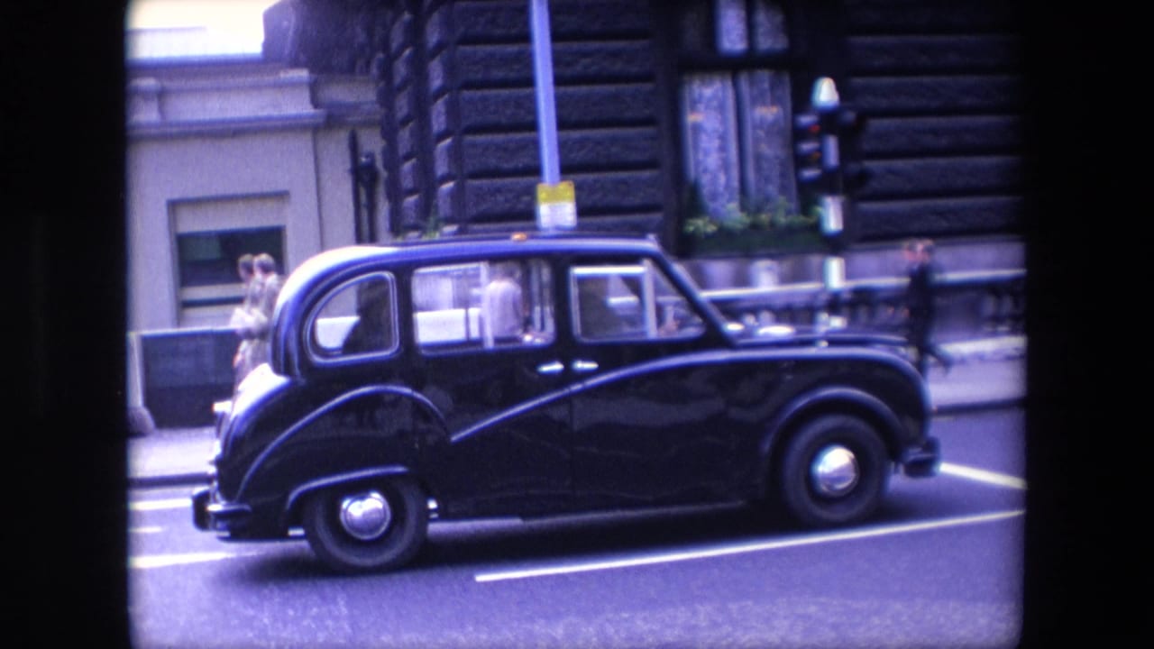 Black taxi stopped at a traffic light on a London city street with pedestrians on the pavement.