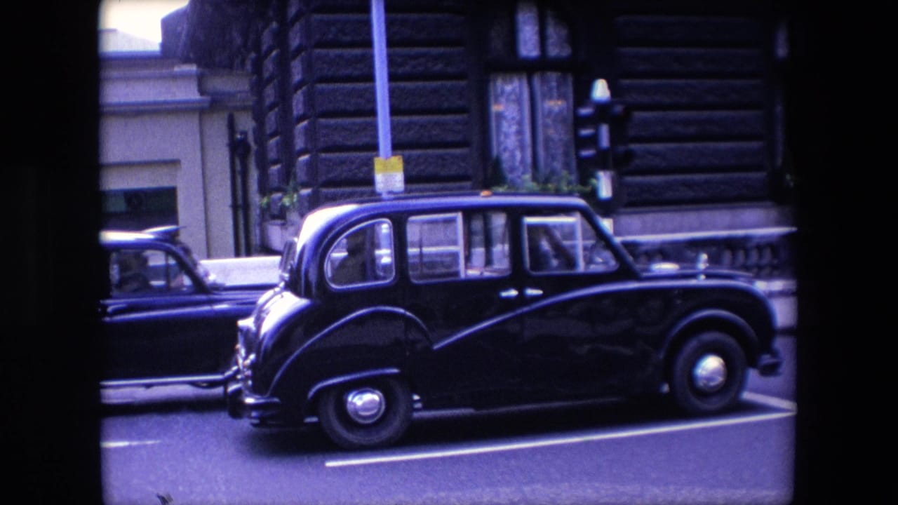 Black taxi beside another dark vehicle at a traffic light on a city street.