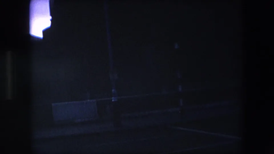 Underexposed 8mm frame from the London clip showing a mostly dark street-side or building-edge view with only a small bright area visible at the upper left.