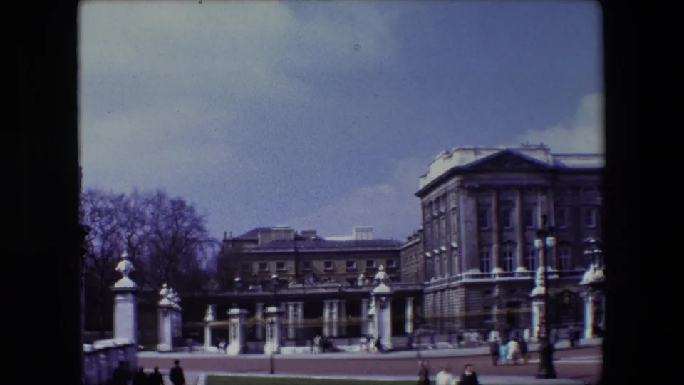 1967 London frame with pedestrians near stone railings and gates, leafless trees, a statue element, and a large formal building under a pale sky.