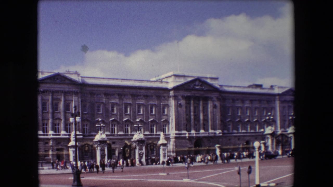 Buckingham Palace facade with tourists gathered near the forecourt gates.