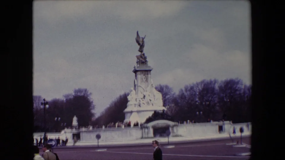 End frame from the 1967 London clip showing the Victoria Memorial across the roadway, with pedestrians at the lower edge and winter trees behind the monument.