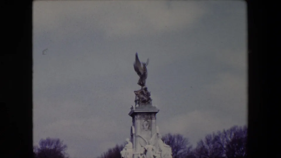 1967 London frame focused higher on the Victoria Memorial, placing the bronze winged figure and marble pedestal against a cloudy gray sky.
