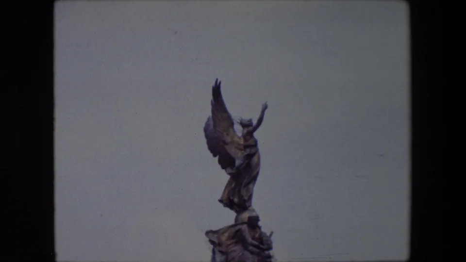 Tight 1967 London frame of the Victoria Memorial's winged figure, with the bronze statue isolated against the cloudy sky and only the upper sculptural base visible.