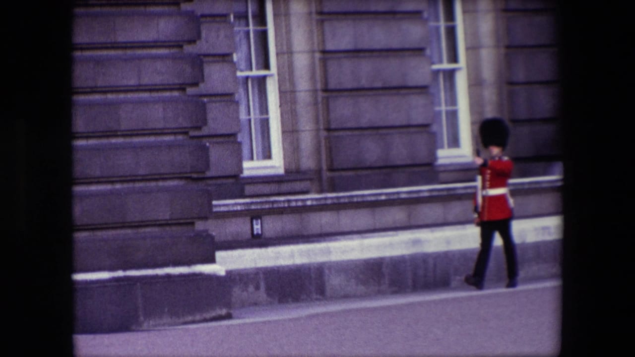 British guard in red uniform marching along a stone building facade.