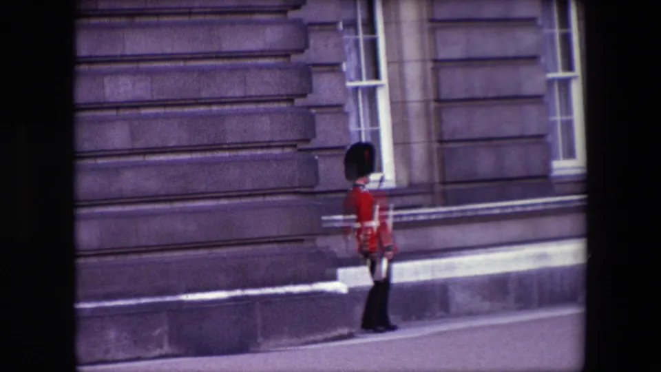 Final 1967 London frame showing the red-coated guard near a sash window, with the handheld 8mm framing emphasizing the stone facade and walkway.