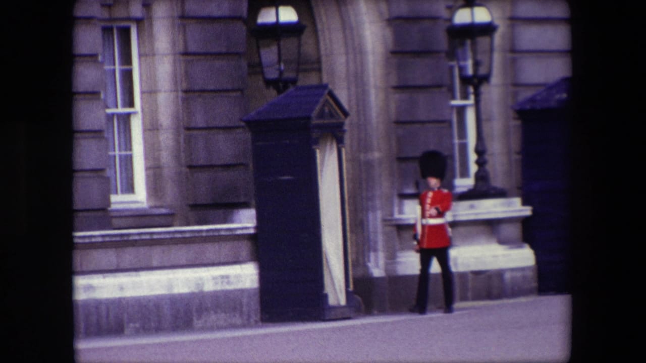 Royal Guard in red ceremonial uniform stands near a dark sentry box outside a stone building.