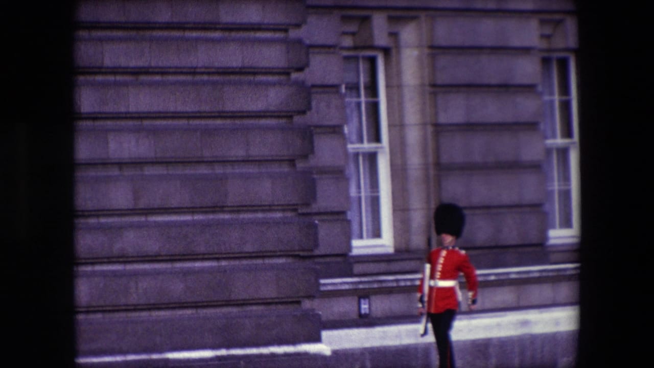 Queen's Guard in red uniform walks along the palace exterior beside tall windows.