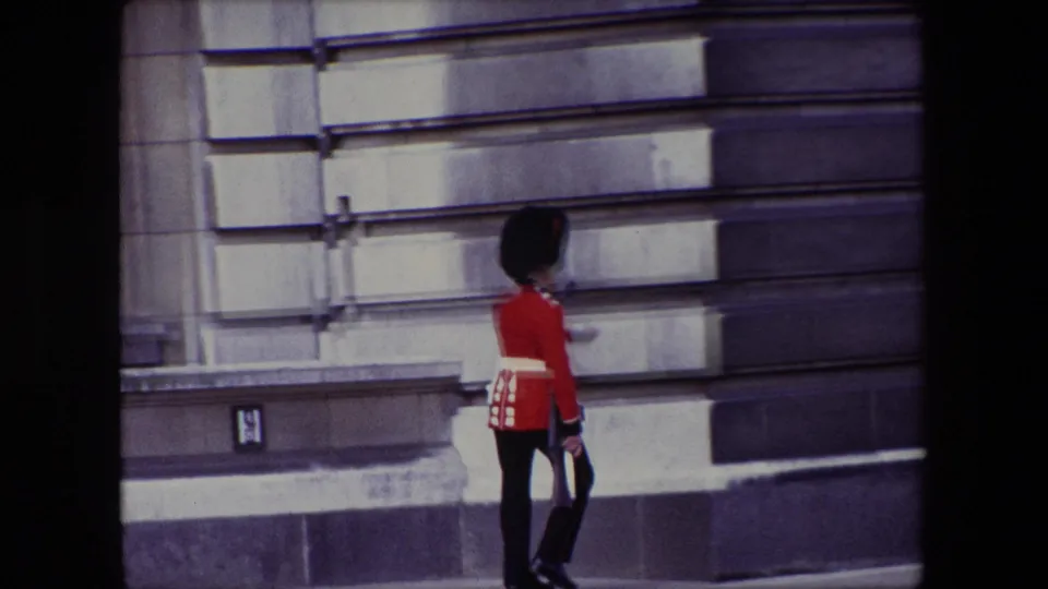 The uniformed guard appears near a stone wall during the turning portion of the march, with the home-movie frame partly shadowed.