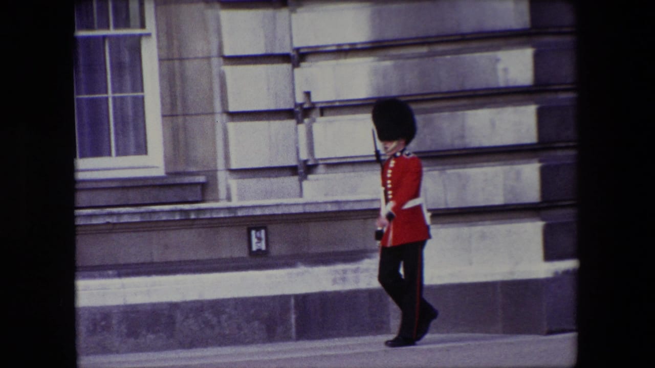 Guard in red ceremonial uniform walking along a stone building.