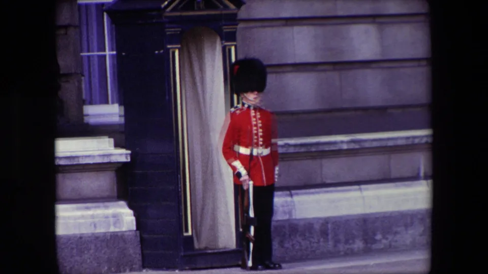 A Queen's Guard stands at attention beside a dark sentry box with pale curtains outside a formal London building, consistent with the supplied 1967 clip metadata.