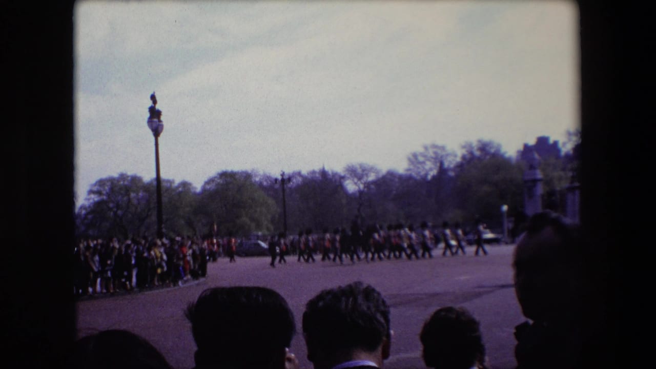 Crowd watches uniformed soldiers marching across a broad paved area.