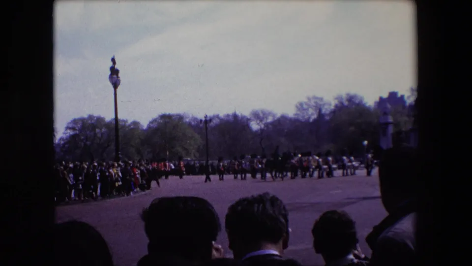 A wide 1967 London home-movie view shows a crowd gathered along a ceremonial route as uniformed soldiers move across the open paved space.