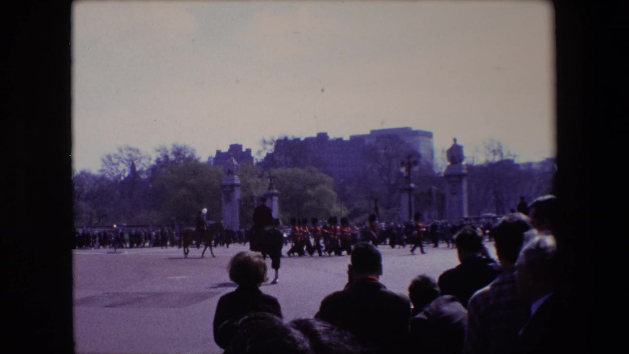 Mounted riders and guards move across a parade ground as spectators watch from the foreground.