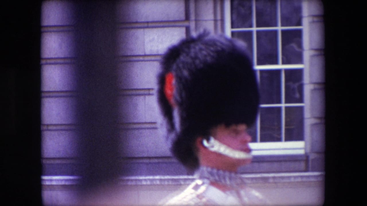 1967 London home-movie frame showing a Queen's Guard in profile near a stone facade and multi-pane window, with soft focus and visible film borders.