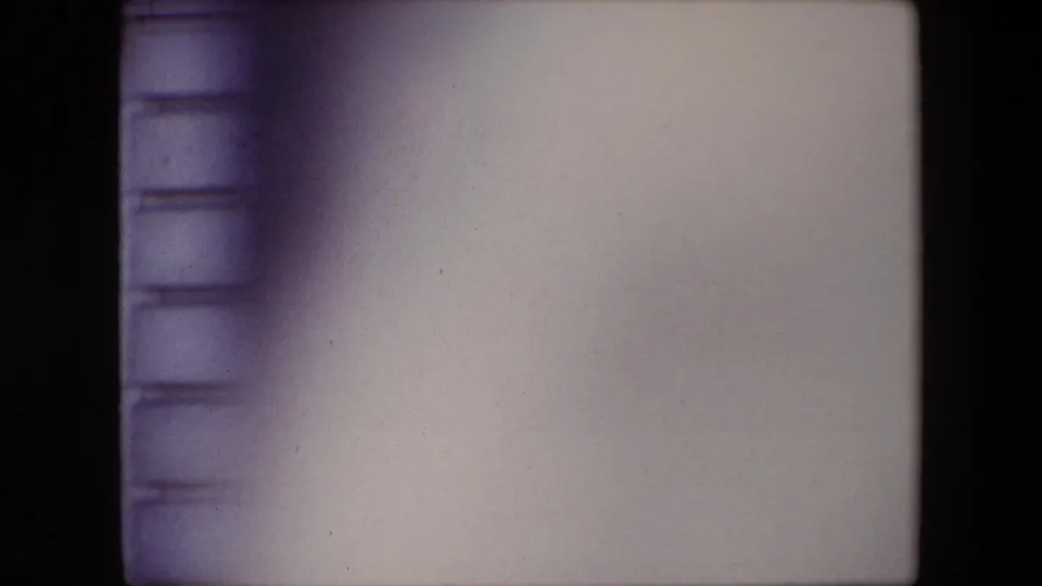 Pale exposed portion of the 8mm frame with dark scan borders and a partial stone wall edge, likely between clearer views of the guard scene.