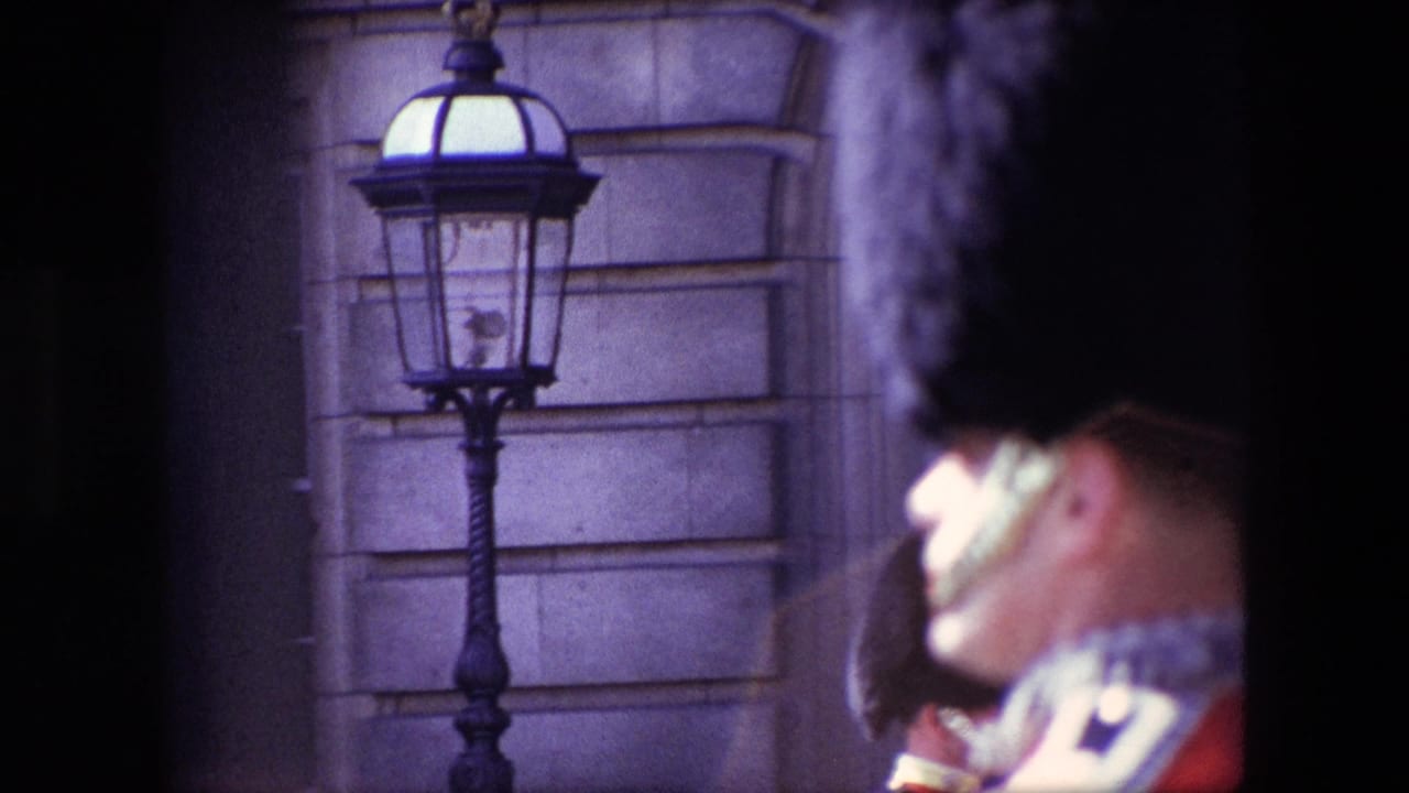 1967 London home-movie frame showing a black palace-style lamp on a stone facade, with a red-uniformed guard partially blurred at the right edge.