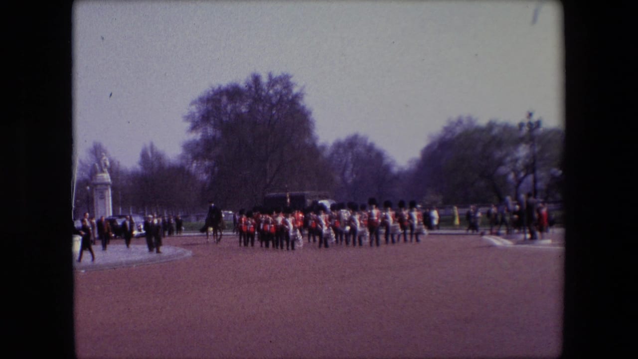 British guards march in formation on a wide path with spectators and trees in the background.