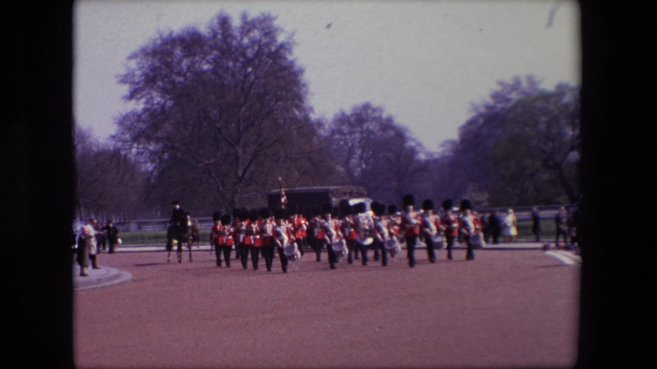 A guards band marches on a broad path with a mounted officer, spectators, and a dark vehicle behind them.