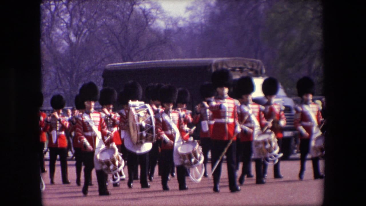 Uniformed marching musicians seen from behind on a broad street with a large vehicle ahead.