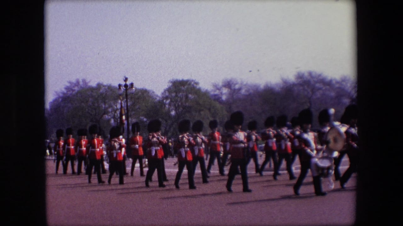 British guards in red uniforms and dark bearskin-style hats march across a broad paved area.