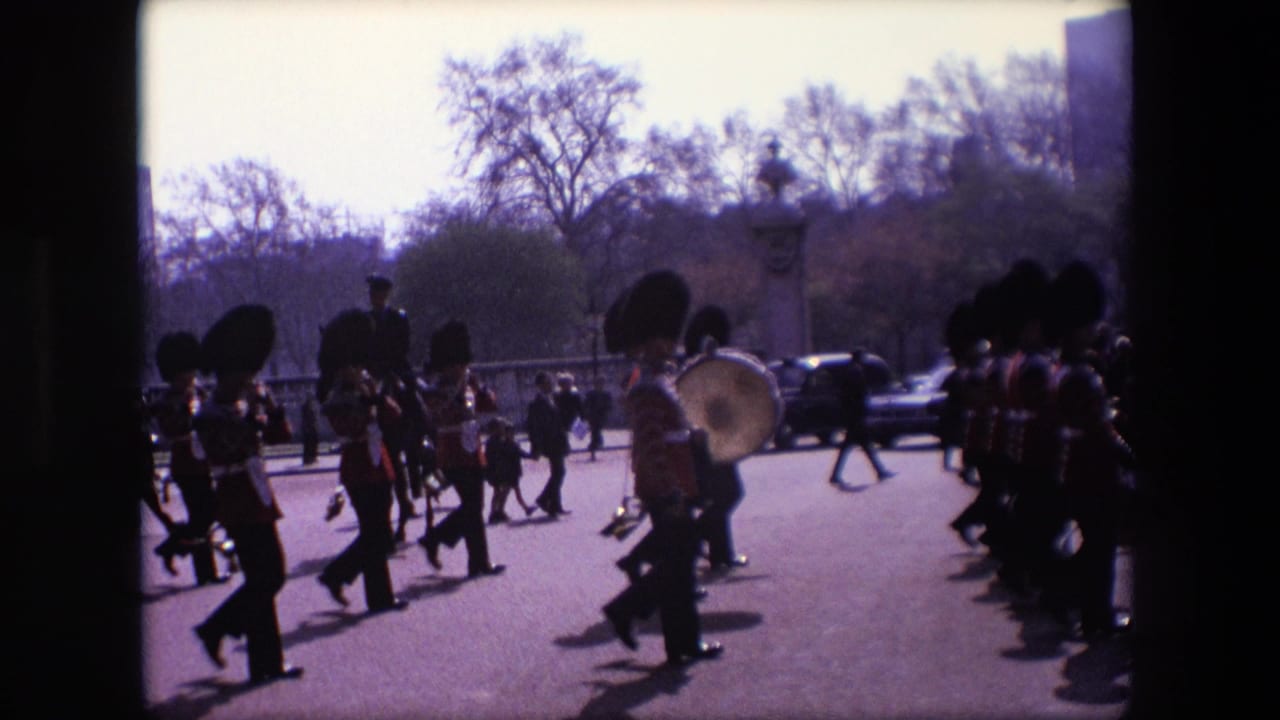 Ceremonial guards and musicians march across the street as people watch nearby.