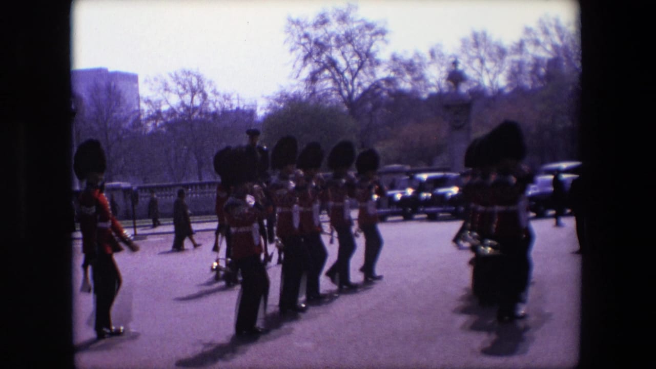 Guards in bearskin hats march across a London roadway as pedestrians and cars appear behind them.