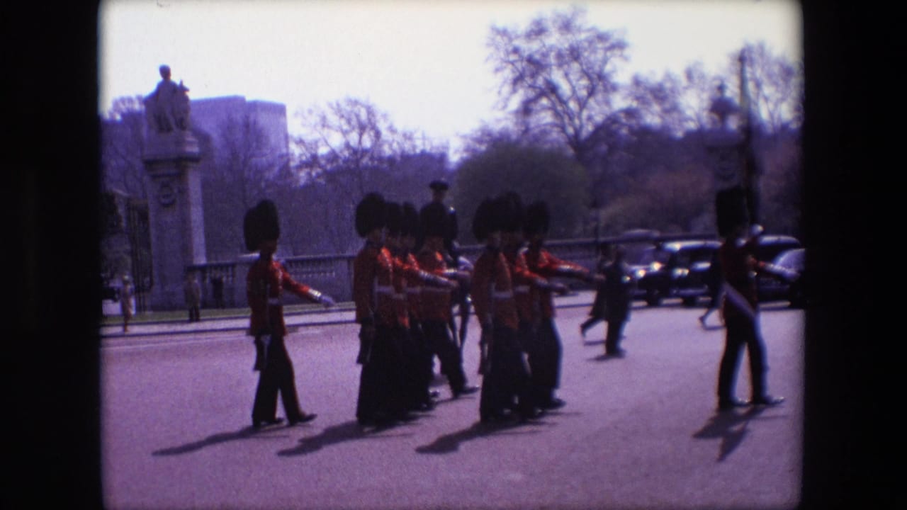 Uniformed guards march along a London street as spectators and cars appear in the background.