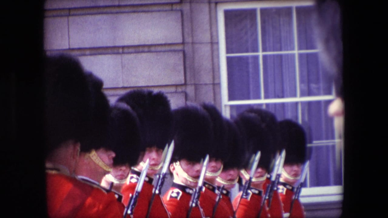 London 1967 home-movie frame showing red-coated ceremonial guards with rifles and bayonets in formation near sash windows on a stone facade.