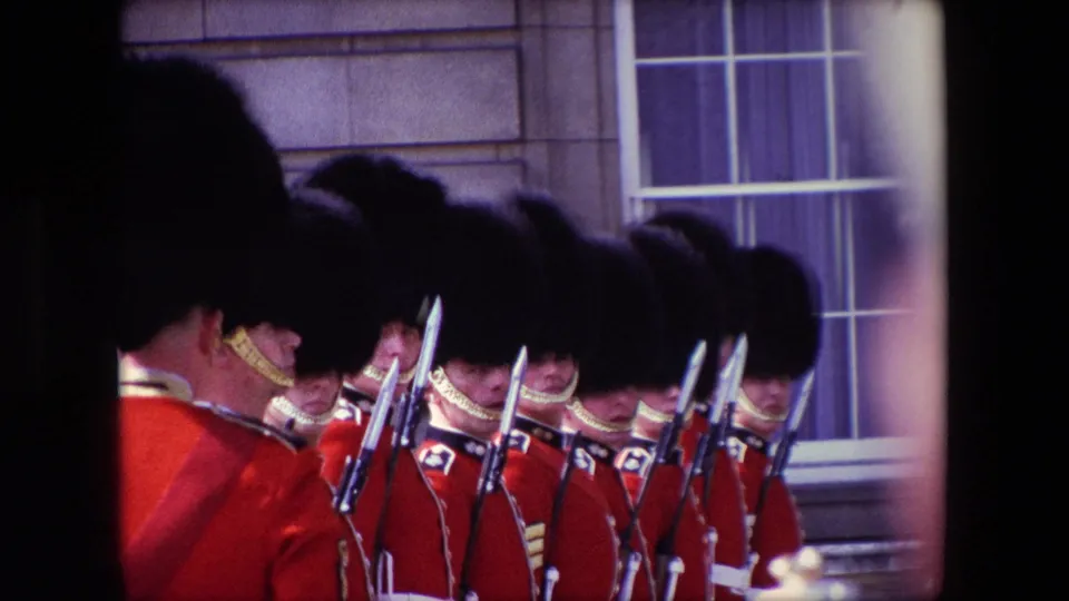 London 1967 home-movie view of ceremonial guards in red uniforms and dark hats, with rifles and bayonets visible through heavy contact-sheet borders.