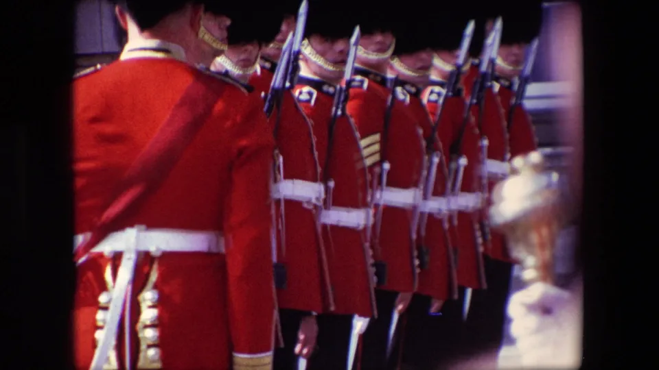 A 1967 London frame shows a rear-facing ceremonial guard in red uniform before a line of guards holding rifles with fixed bayonets.