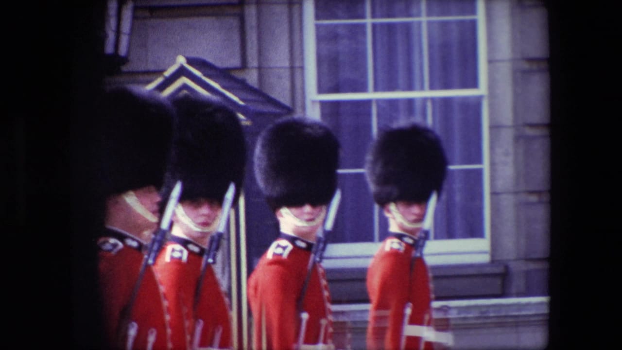 British guards in red uniforms standing at attention outside a stone building.