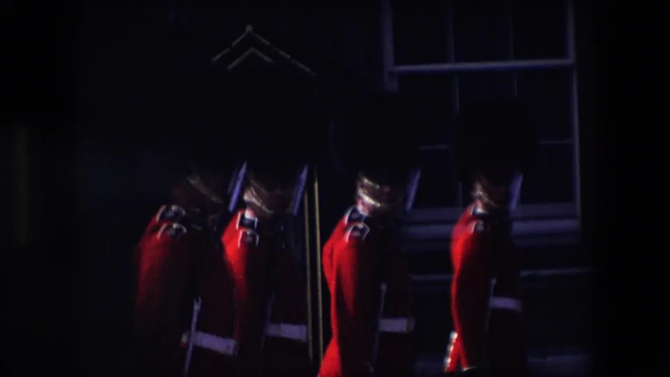 Underexposed 8mm frame with partial silhouettes and glimpses of red-uniformed guards near a building exterior in London.