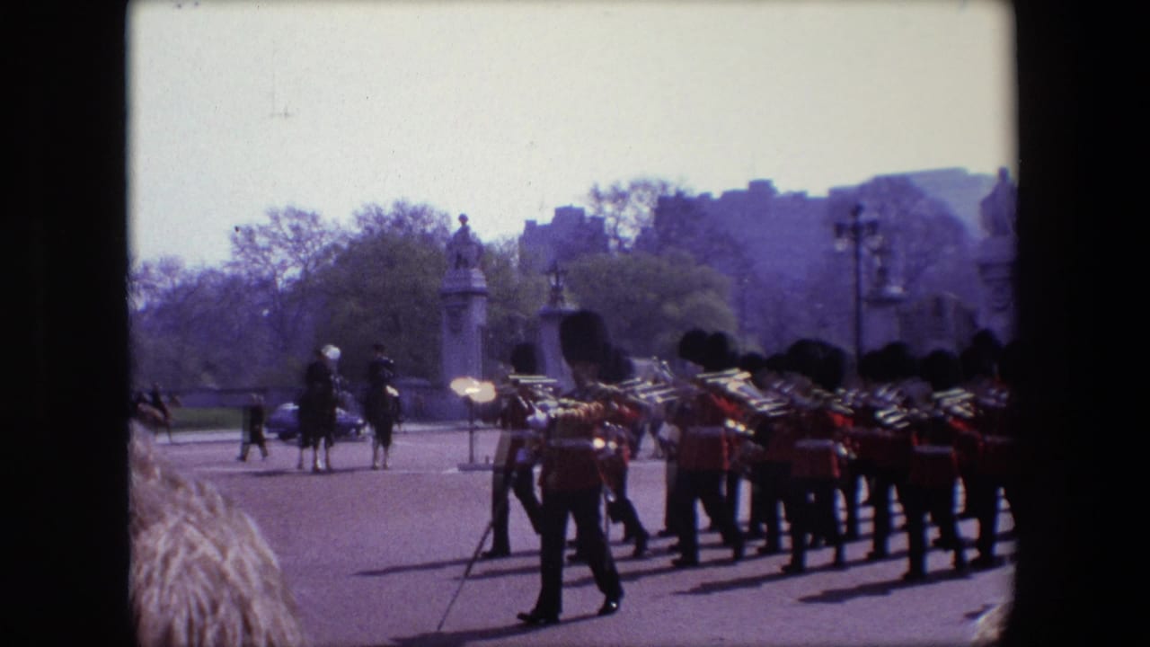 Royal Guard marching band crossing a broad London roadway with brass instruments and mounted figures in the distance.