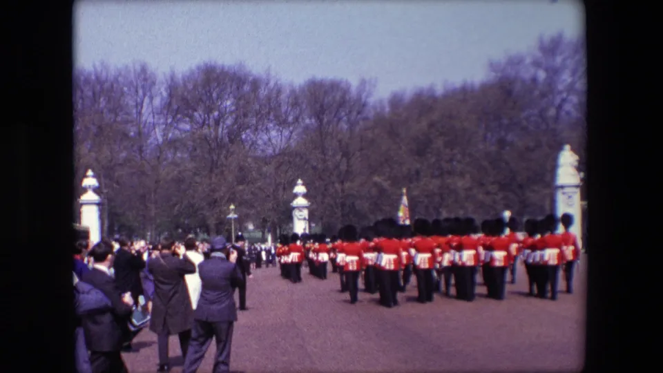 1967 London home-movie view of red-uniformed guards marching away from the camera while spectators stand along the side of a broad public space.