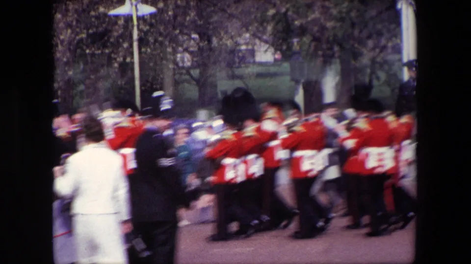 Motion blur captures the red-uniformed band in movement through the London street, with spectators and uniformed figures partly visible along the parade route.